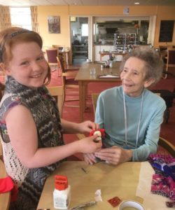 A young girl and elderly woman smile as they enjoy making puppets together in Indigo Moon Theatre's workshop.